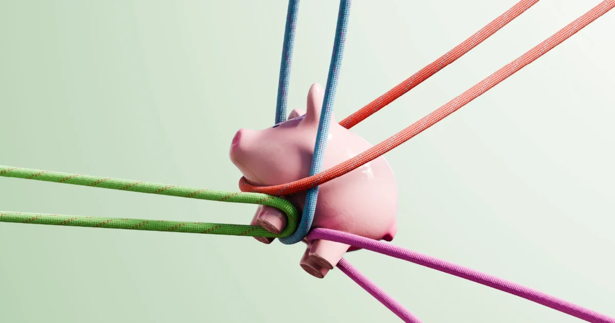 A pink piggy bank pulled tightly by colorful ropes against a pale background.