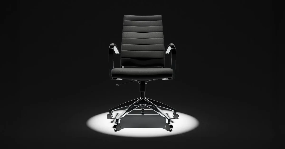 Black office chair with chrome base and armrests, spotlighted against a dark background