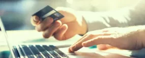 Man typing on computer while holding a credit card