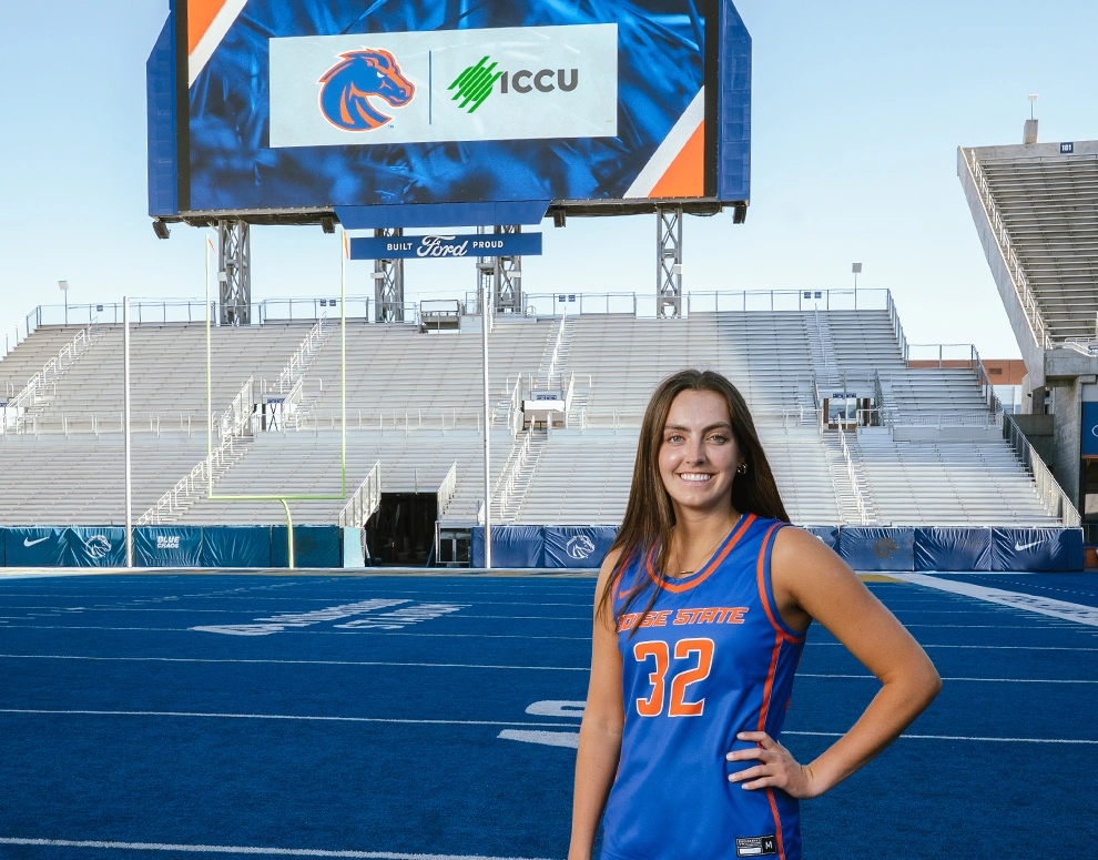 Natalie Pasco poses in front of a large jumbotron displaying the Boise State Broncos and ICCU logos.